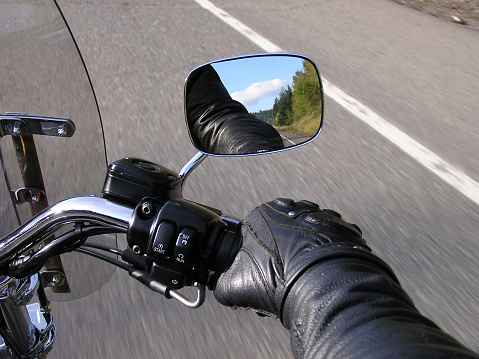 Motorcyclist's hand on throttle.  Beautiful blue sky and greenery are visible in side-mirror.  Point of focus on grip switches and side-mirror.See similar shot of this image: