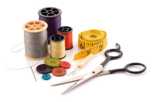 A collection of sewing tools and supplies in a sewing kit, isolated on a white background. Items include color threads, buttons, needle, tape measure, scissors, and seam ripper, equipment and work tools needed for a typical fabric sewing project.