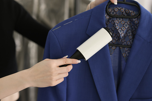 Woman removes pellets from blue woolen coat using fabric roller brush. Young employee takes care of conditions of clothes at work in dry cleaning