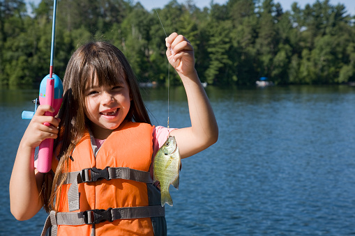 A little girl is holding up her sunfish catch.  With copyspace.