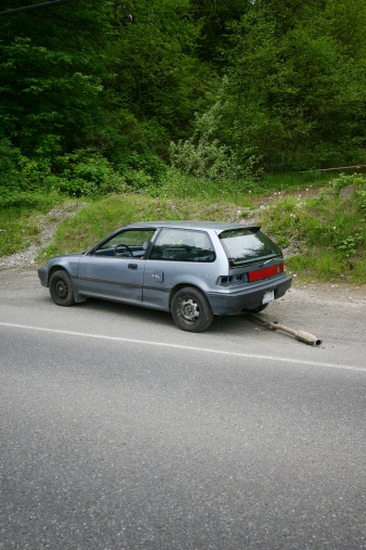 A broken down car sits abandoned along a country road.