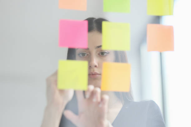 istock Brunette woman puts sticky notes on glass wall in office 1722349250