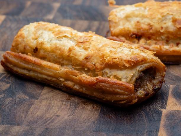 Sausage roll on a wooden chopping board, crispy golden flaky pastry Sausage roll on a wooden chopping board, crispy golden flaky pastry filled with pork sausage meat sausage roll stock pictures, royalty-free photos & images