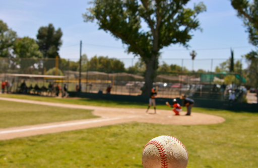 Leftie batter up in baseball game to go against other team in Little League game in out of focus background with old baseball in foreground focus