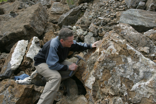geologist scientist looking at rock outcrop with his hammer