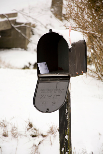 A black mailbox is open, with flag up and mail waiting to be delivered.  It is topped by snow.