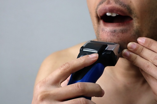 Close-up of a Japanese man shaving his beard with an electric shaver