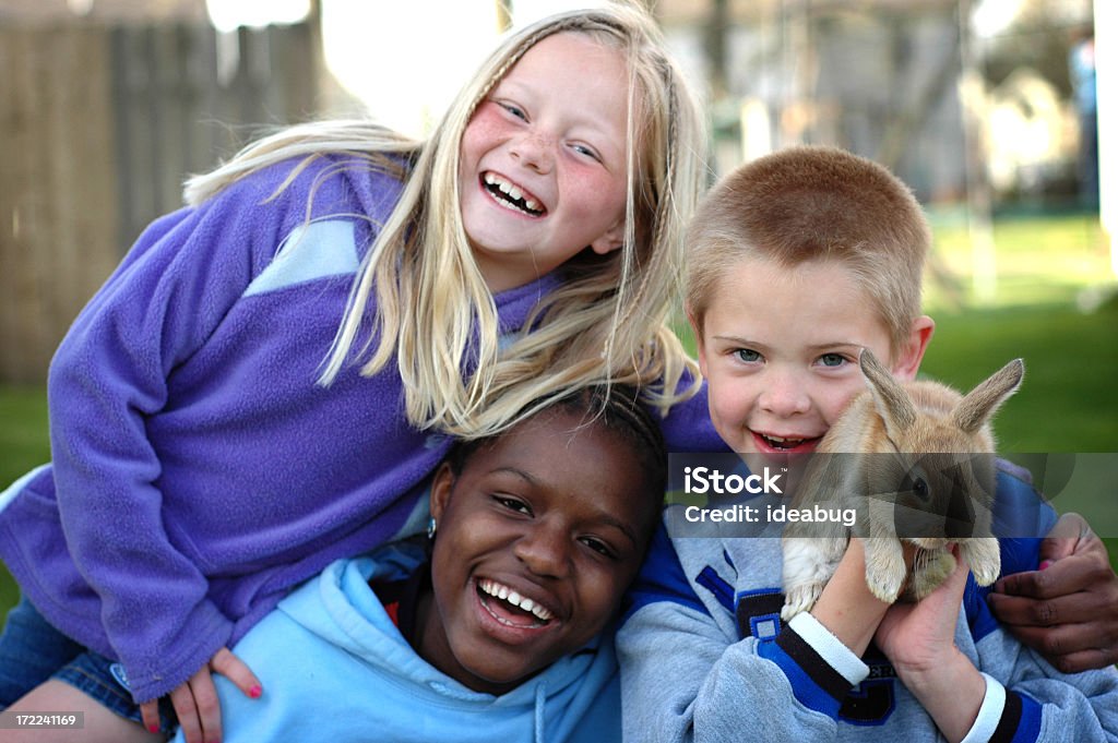 Two Girls and a Boy Laughing Together Outside with Bunny Color photo of three adorable kids and a bunny having fun and laughing together outside!  They are siblings by adoption. Adoption Stock Photo