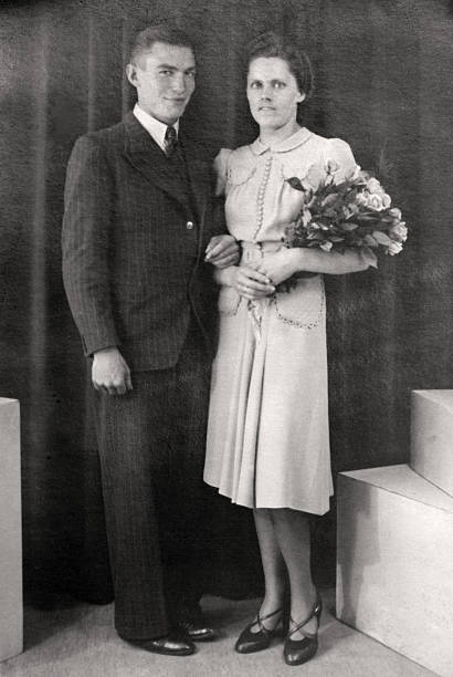 Just married couple in the thirties Wedded couple with flowers in front of a curtain. wedding photos stock pictures, royalty-free photos & images