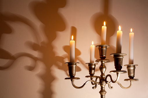 Lit candles in a candelabra making a shadow on the wall