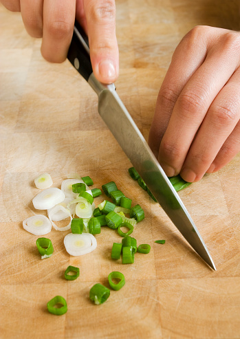 A woman chopping a bunch of spring onions on a wooden chopping board.