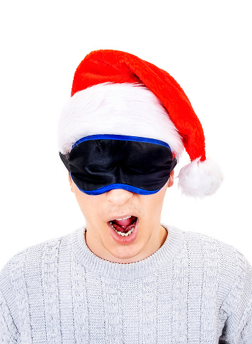 Young Man in Santa Hat and Sleep Mask is Yawning on the White Background closeup