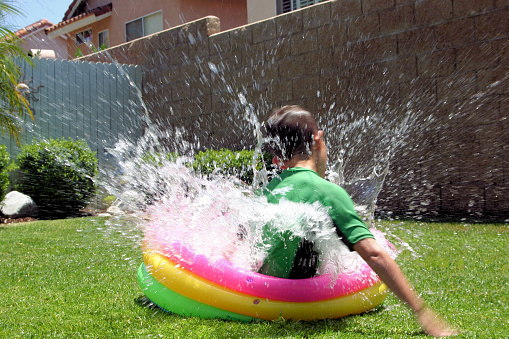 young boy splashing in a small pool to keep cool on a warm summer dayMore of these children