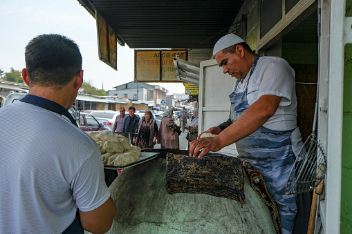 Osh, Kyrgyzstan - October 6, 2023: A man making samsas in a clay oven at the Jayma Bazaar in Osh, Kyrgyzstan.