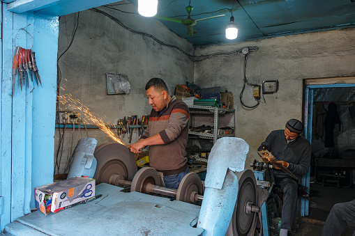Osh, Kyrgyzstan - October 6, 2023: Men sharpening knives at the Jayma Bazaar in Osh, Kyrgyzstan.