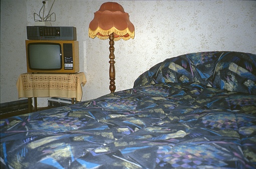 Germany, 1980. Bedroom with bedspread, TV, radio and floor lamp.