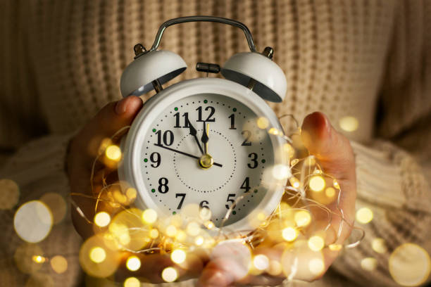 cuenta atrás mágica para la medianoche. las manos de las mujeres en suéter sostienen el despertador con flechas de los últimos minutos a 12 en la esfera del reloj. esperando la llegada del año nuevo y las vacaciones. - new years eve clock time arrow 12 hours fotografías e imágenes de stock