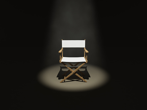 Front side of a wooden / white director's chair under the spot light.
