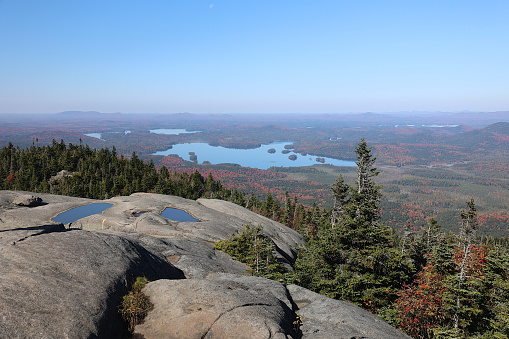A beautiful vista from the summit of Ampersand mountain in Adirondack state park.  This summit is not in the high peak region, but presents landscapes that include many lakes.\n\nThis photo was taken in early October when fall foliage was deemed to be at peak colors.