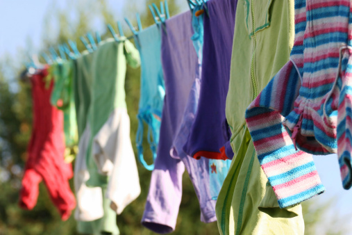 Young woman hanging up laundry on a clothesline with a blue sky background.