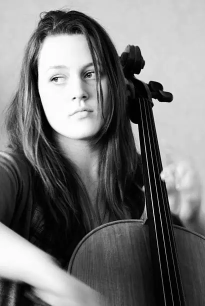High key, black and white image of a teenage cellist playing her cello. With motion blur on hands. 