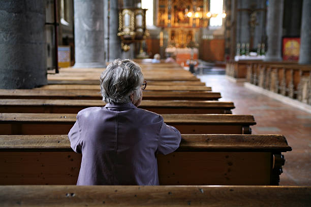 Older woman praying in an almost empty church, rear view stock photo
