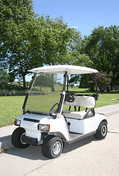White golf cart parked by the side of the golf course stock photo