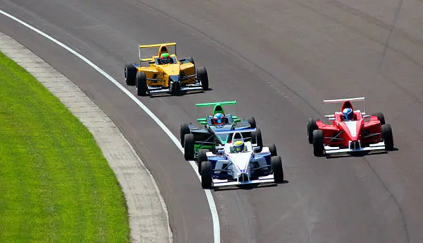 four open wheel cars racing around a turn at the Indianapolis Motor Speedway in Speedway, Indiana