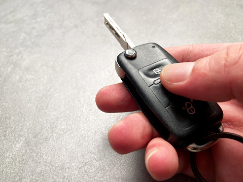 Hand holding car key and pressing push button