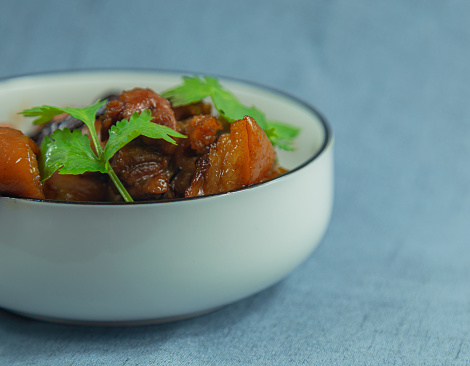 The shot is of a traditional Chinese dish, braised pork, with a blank frame left in the composition of the shot. White porcelain bowl with tender green cilantro leaves on top of the braised pork. Individual preparation of traditional Chinese home cooking.