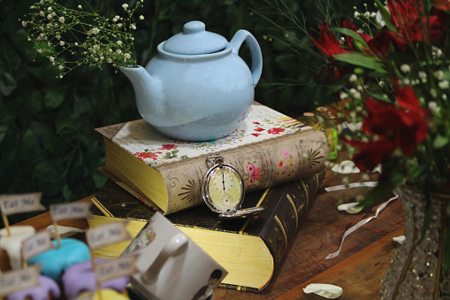 Fantasy themed birthday table decoration. Teapot, books, flowers and clock. With mini cakes with selective focus.