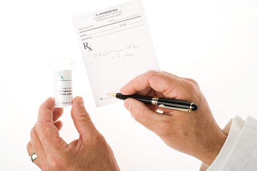 Doctor's writing a prescription with a pen.  Left hand holding a empty labelled bottle. 