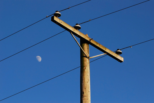 Hydro pole and lines cut through the view of blue sky