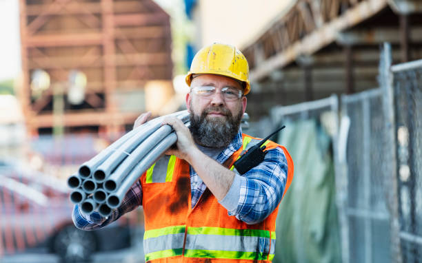 construction worker carrying pipes on shoulder - werkhelm fotos stockfoto's en -beelden