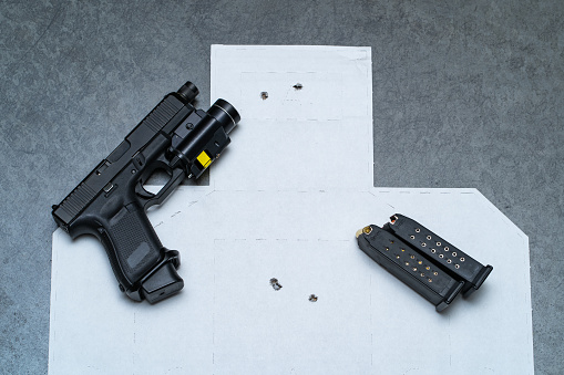 Pistol with red laser sight and ammunition magazine on the paper target with bullet holes , high quality photo