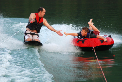 A ten year old boy reaching for his Dad's hand as they tube and kneebaord tandem