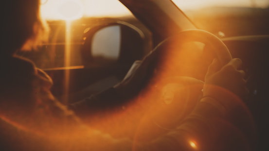 In the golden embrace of sunset,a close-up reveals the midsection of a man driving,with a radiant lens flare adding an enchanting touch to his journey.