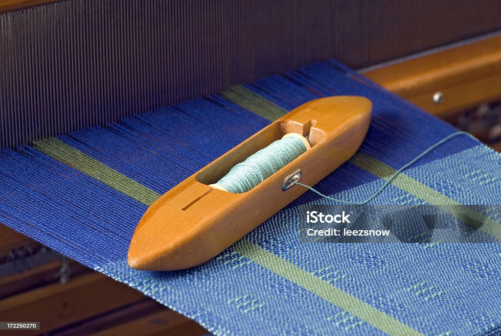 Weaving Blue Yarn on a Loom Weaving shuttle with bobbin and thread sitting on a project in process on a loom.  Narrow dof with focus near center of shuttle.More weaving and loom shots: Single Object Stock Photo