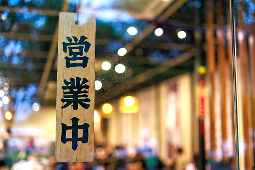 A Chinese character 'open' sign on a restaurant hangs on the door at the entrance.