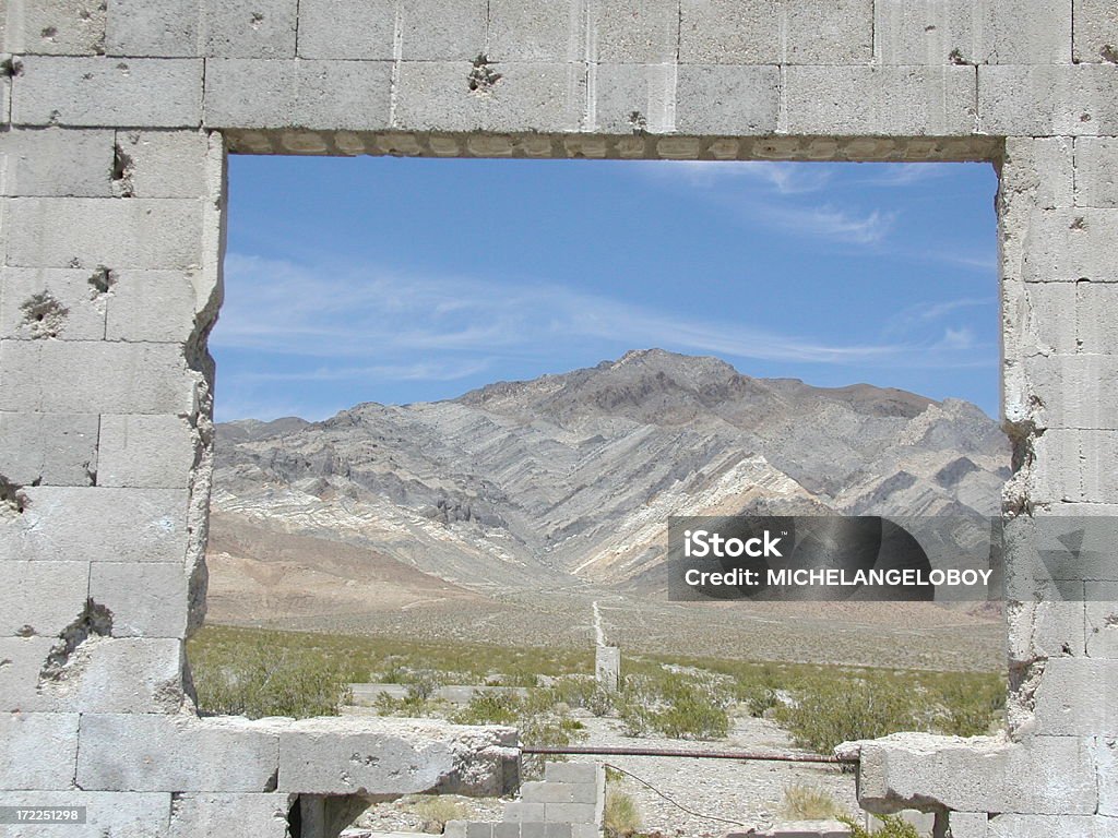 Shotgun Brick Wall & Window Old falling down building with view thru window. Desert scene of mountains and blue sky. Bible Stock Photo