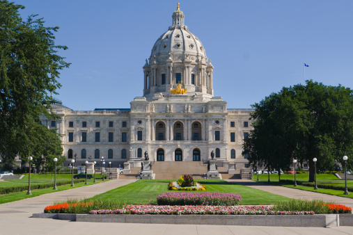 Front entrance approach of the Minnesota State Capitol building in St. Paul, Minnesota, USA, a facility for government legislation. The architectural classical style of the monumental domed building exterior facade, formal gardens, flower beds, lawns and grounds are a tourist travel location and famous place.