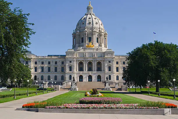 Front entrance approach of the Minnesota State Capitol building in St. Paul, Minnesota, USA, a facility for government legislation. The architectural classical style of the monumental domed building exterior facade, formal gardens, flower beds, lawns and grounds are a tourist travel location and famous place.