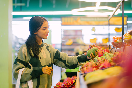 Young adult asian woman bbuying fruits at supermarket. Sustainability Lifestyle.