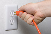 A hand unplugging an orange cord from a white outlet