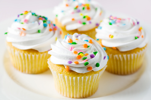 Cupcakes with white frosting swirls and colorful confetti.  Shallow DOF.