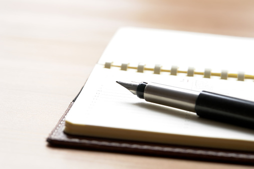 Empty, opened spiral leather notebook with pen lying on it. Wooden table, selective focus, horizontal.