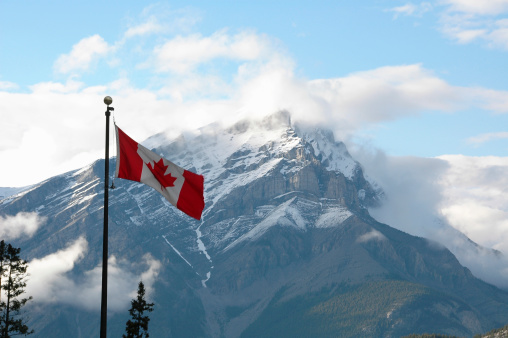 A Canadian Flag flies tall over a mountain outside of Banff, Alberta.
