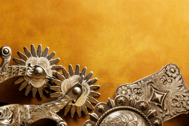 A pair of silver spurs and two silver belt buckles on a leather surface.