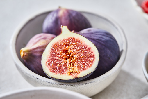 Beautiful ripe figs in a bowl. Healthy granola muesli oatmeal for breakfast, preparation with fresh organic fruit, nuts and grains, at a white granite table in a modern white kitchen, representing a wellbeing and a healthy lifestyle, city life, fast life, healthy habits and smart eating, nutrient rich food, an image with a copy space