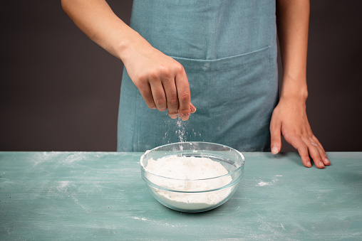 Baker sprinkles salt into a bowl with flour, prepare dough for artisan bread or pizza, ingredients for food, baking pastry